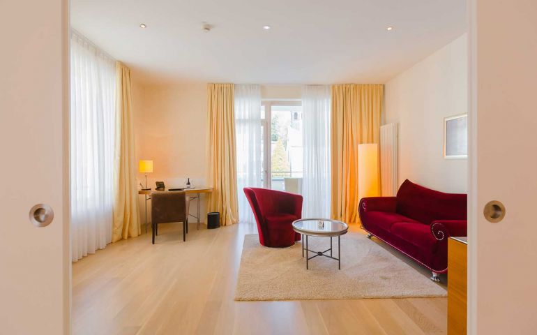 Blick durch die offenen Schiebetür auf einen großzügigen Wohnbereich mit Arbeitsecke und rotem Sofa in einer Deluxe-Suite im Suitenhotel in Baden-Baden