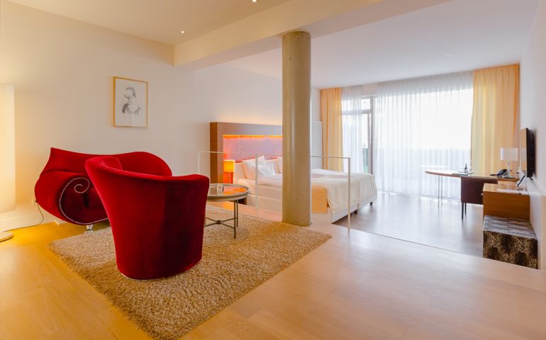 Aufnahme vom Wohnbereich mit roter Samtganitur und dem tiefergelegten Schlafbereich im Suitenhotel in Baden-Baden