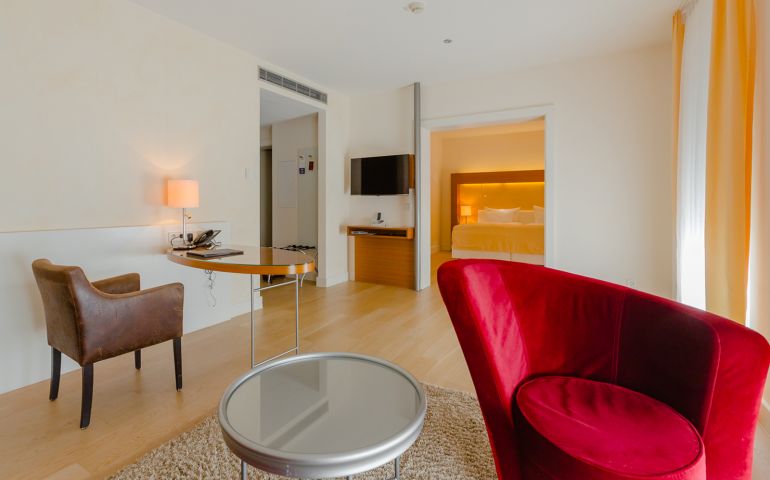Aufnahme über einen roten geschwungenen Sessel und den Arbeitsbereich bis ins Schlafzimmer einer Suite in Suitenhotel in Baden-Baden