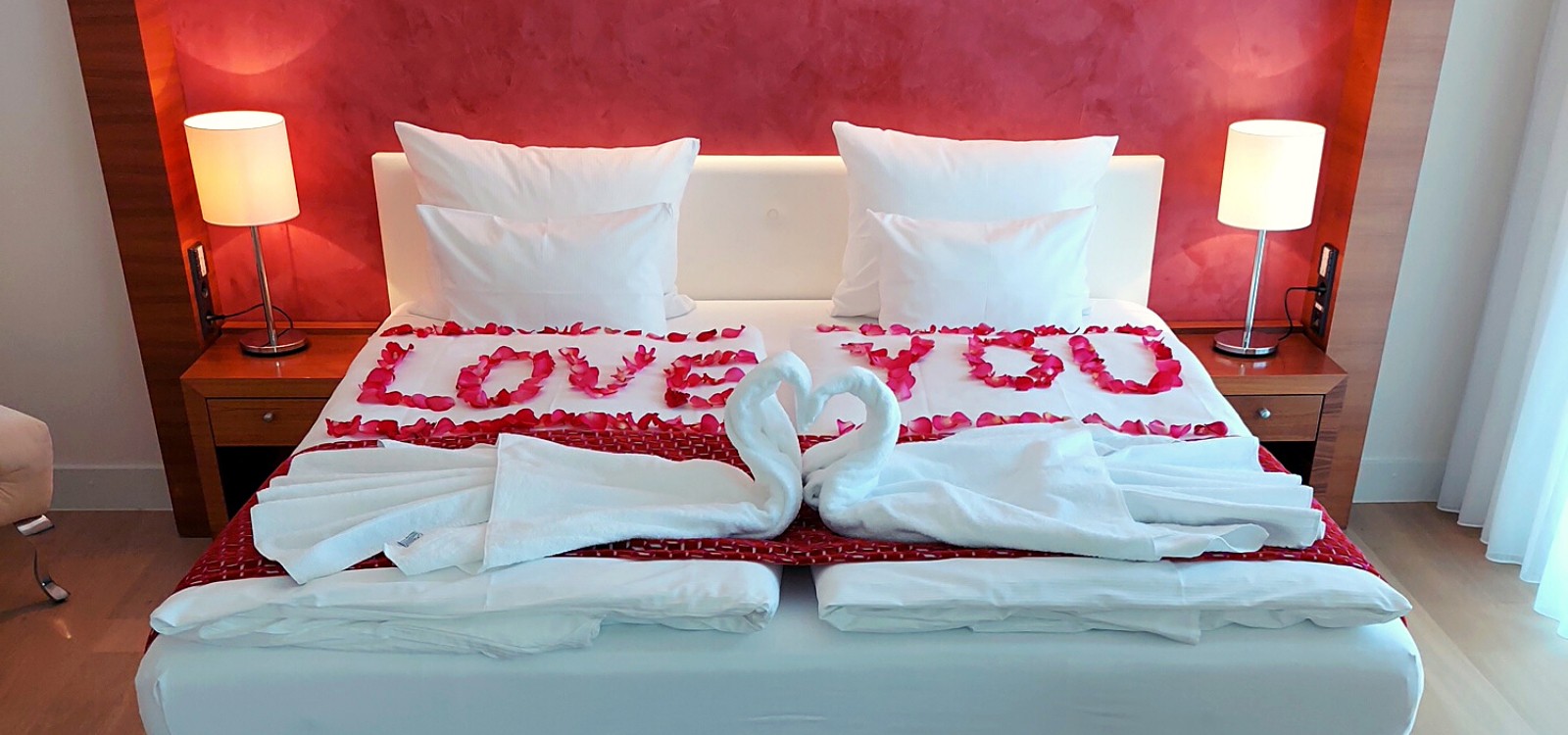 Ein romantisches Arrangement mit Rosenblättern auf dem Bett und zwei aus Handtüchern gefalteten Schwänen im Hotel in Baden-Baden