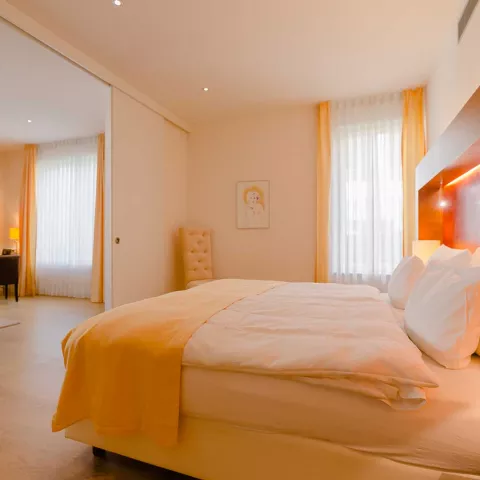 Beleuchtetes Doppelbett in einem großen Schlafzimmer mit anliegenden Wohnzimmer