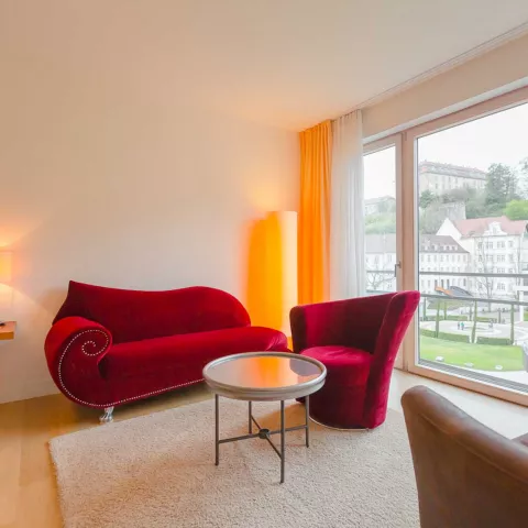Rote Couch in einer Suite neben einem großen Fenster mit Parkblick
