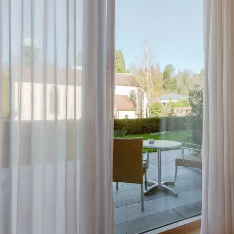Ein Blick durch die offenen Vorhänge am Fenster auf die Gartenterrasse