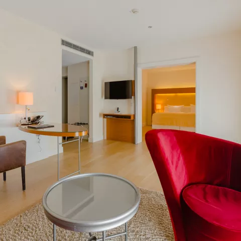 Nahaufnahme eines roten Stuhls mit Fernseher, Tisch und Bett im Hintergrund