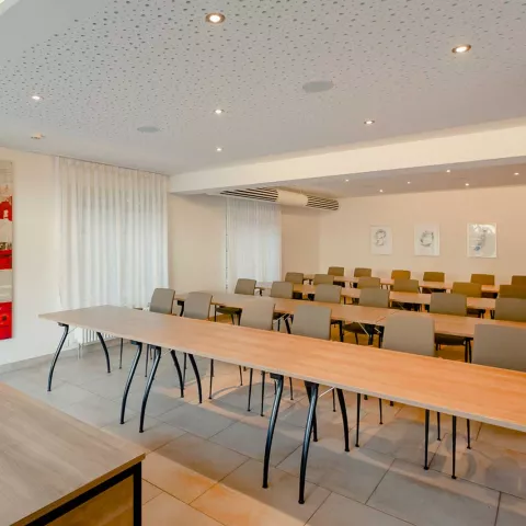 Ein heller Tagungsraum mit ein paar langen Holztischen und bequemen Stühlen