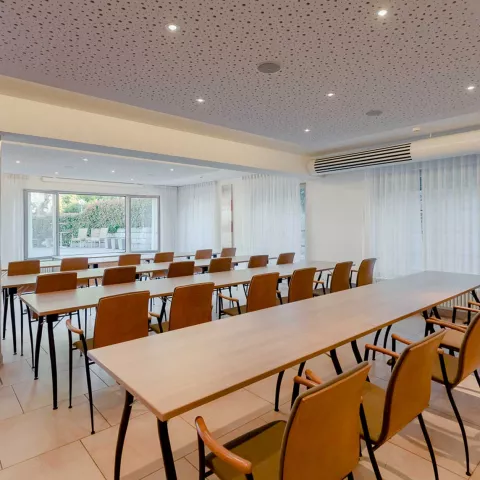 Ein heller Tagungsraum mit vier langen Holztischen und bequemen Stühlen