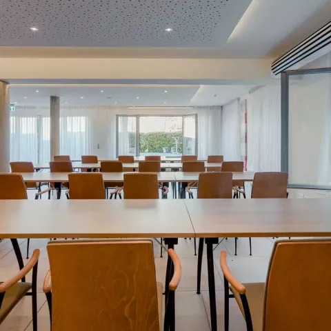 Holztische mit Stühlen in einem Tagungsraum mit großen Fenstern