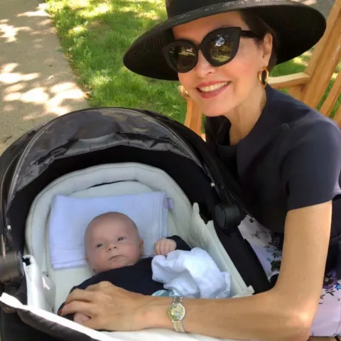 Eine Frau hält die Hand eines Babys, welches in einem Kinderwagen liegt