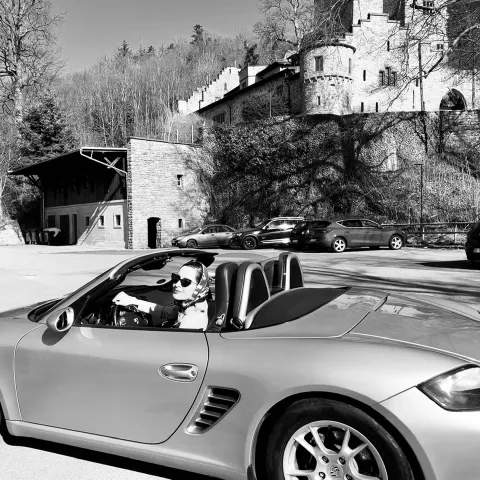 Ein Schwarz-Weiß-Bild von einer Frau in einem Cabrio vor einer Burg