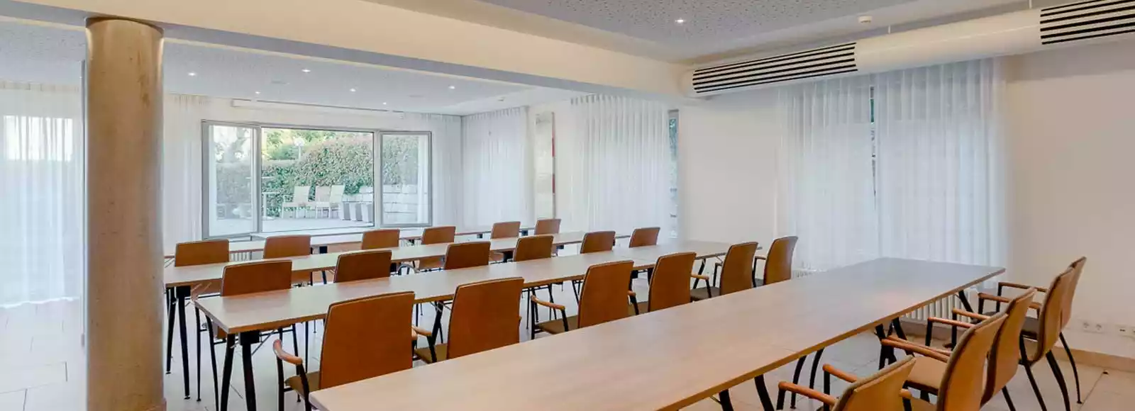 Großer Tagungsraum mit langen Holztischen und vielen Fenstern