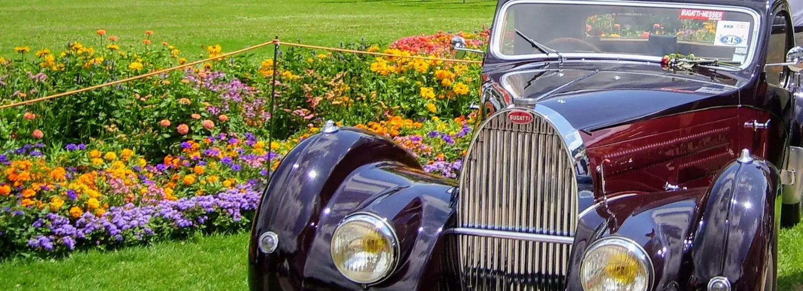 Ein Oldtimer steht im Kurpark vor einem Blumenbeet